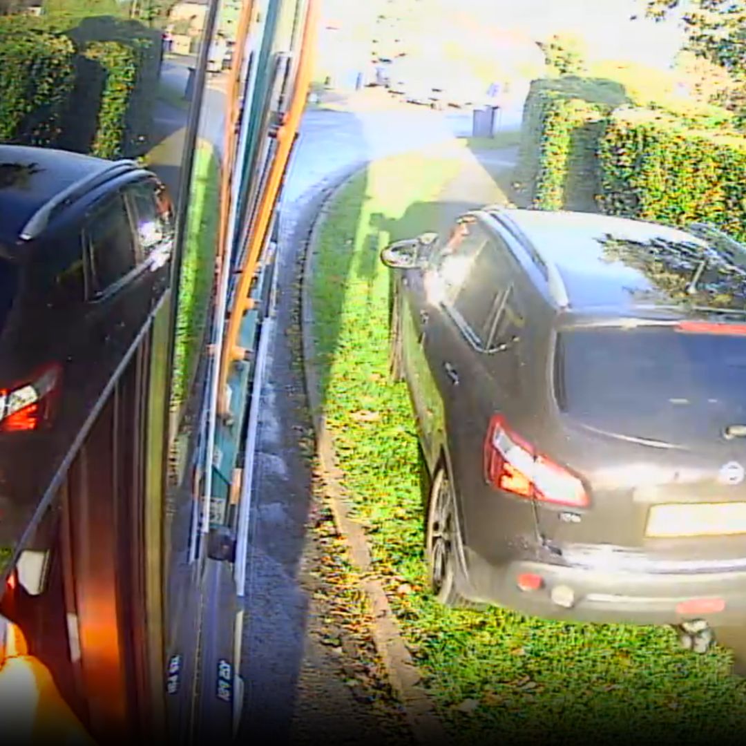 A black car mounting a pavement and grass verge to get ahead of the Ubico waste and recycling vehicle.