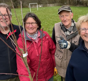 People in the community at an open space smiling and holding a tree