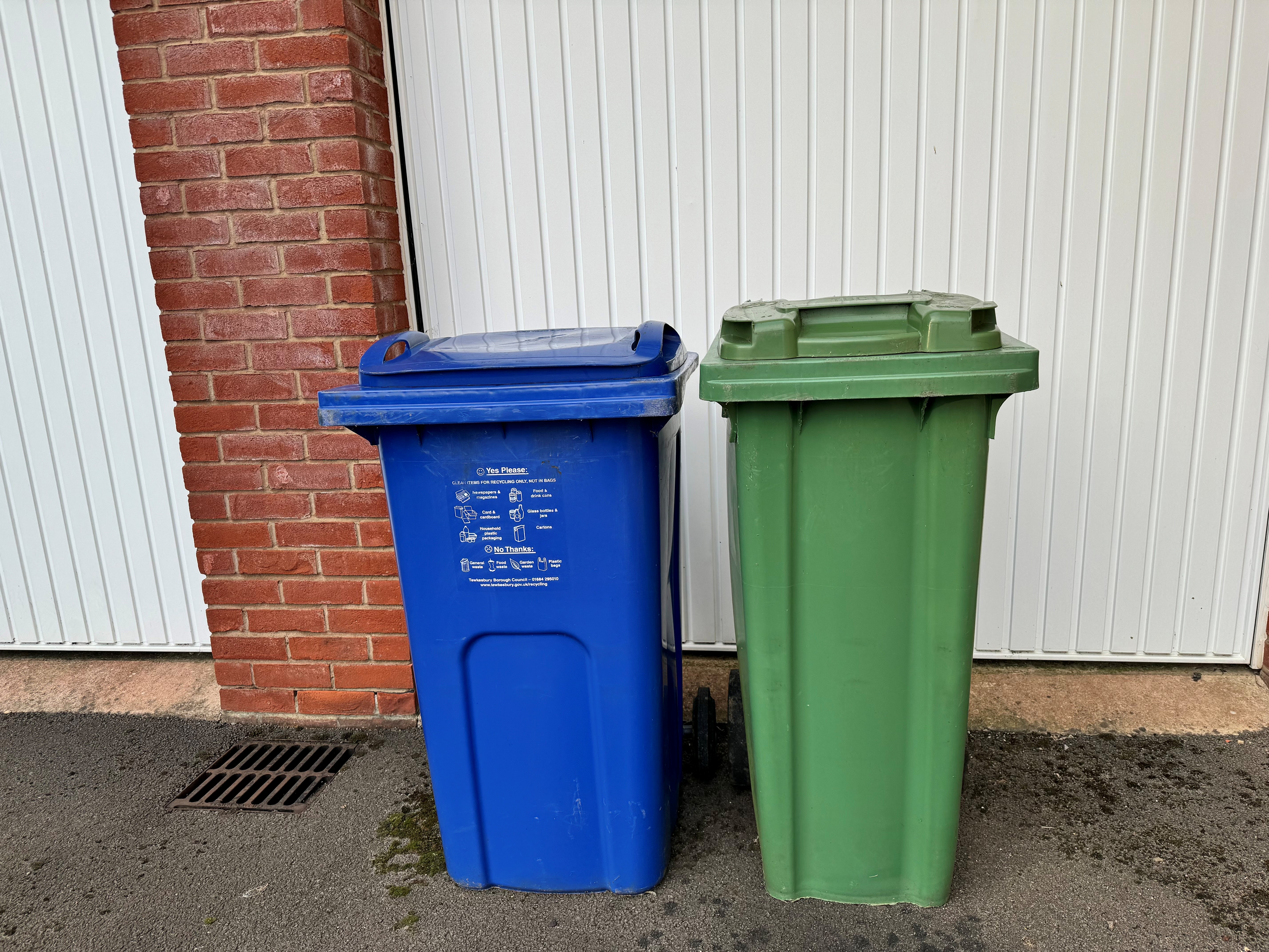 a set of garage doors with two Tewkesbury Borough Council bins, one blue recycling bin and one smaller green general waste bin