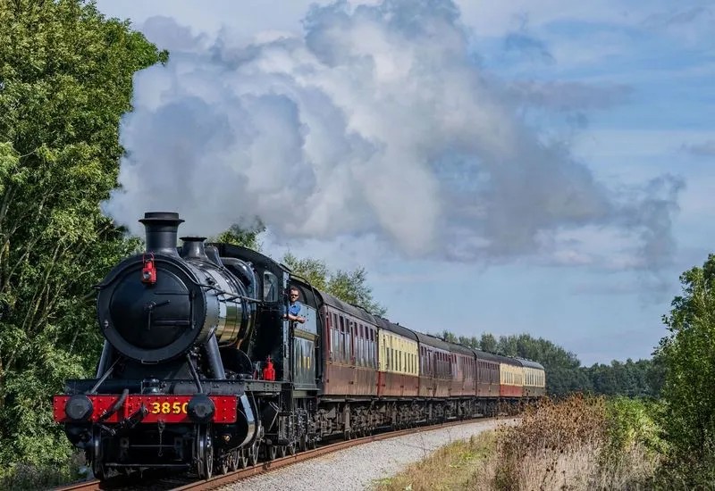 GWR steam engine in motion with clouds of steam against a light blue sky