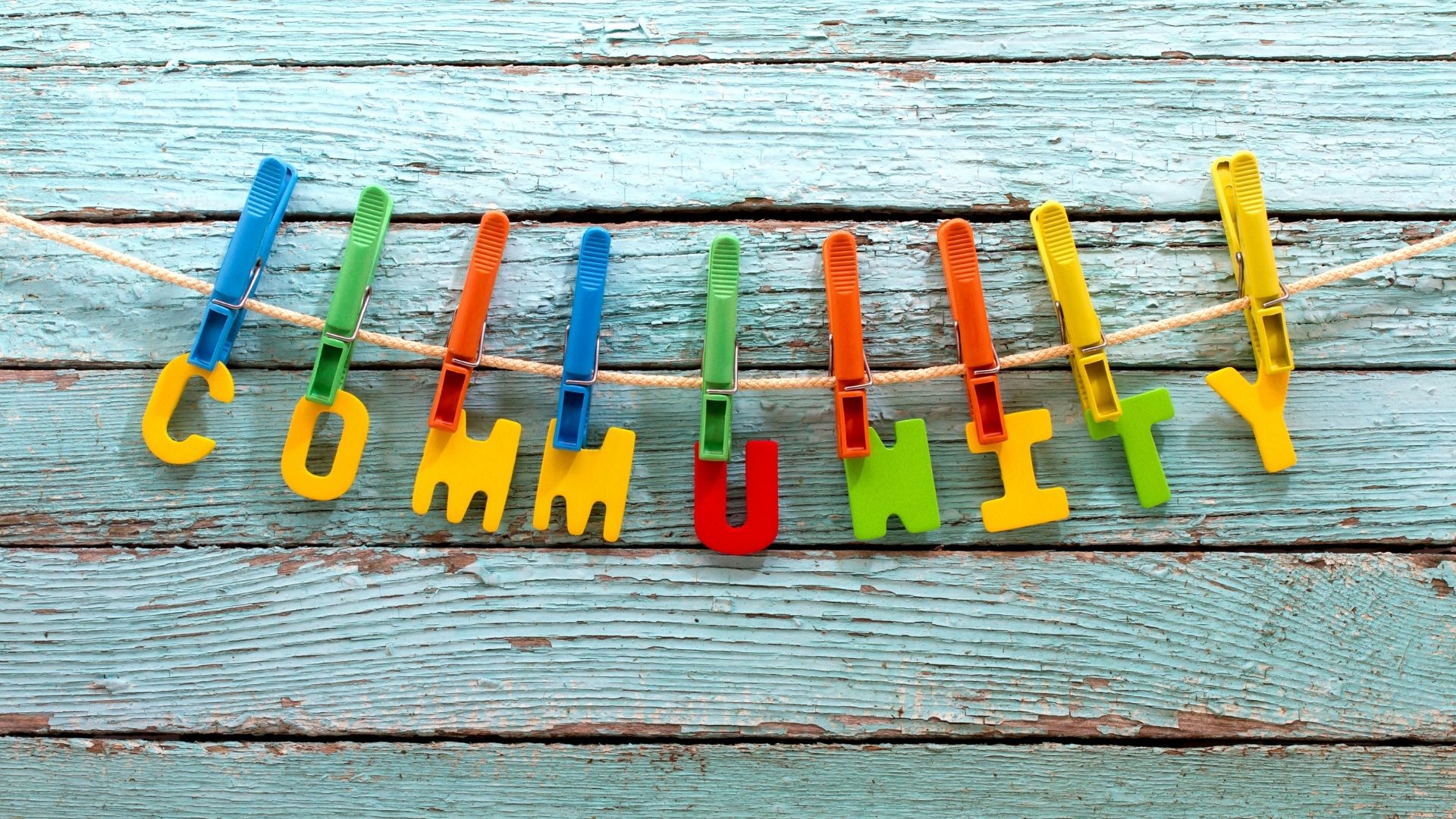 Wooden background with brightly coloured letters hanging on a peg board - making up the word 'community'