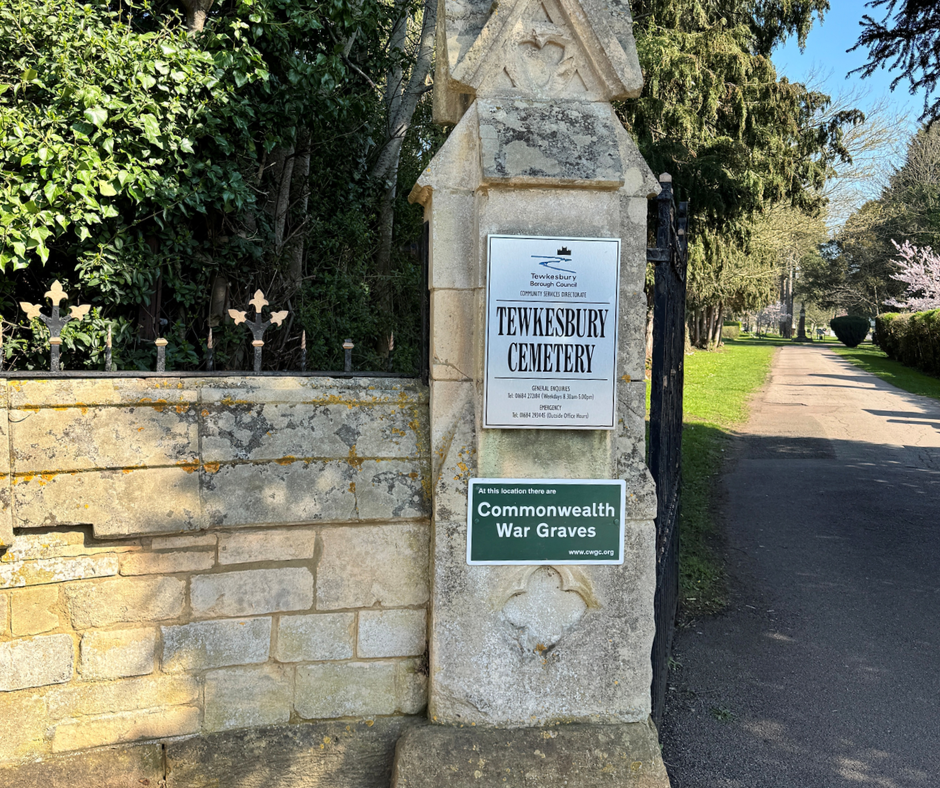 a Cotswold stone wall with iron railings form part of the entrance to Tewkesbury Cemetery. a path is to the right hand side
