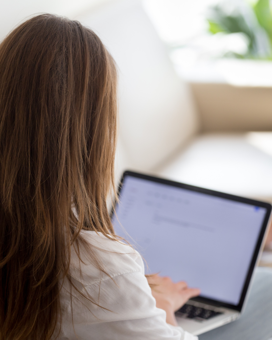 a female is looking at her laptop screen typing.